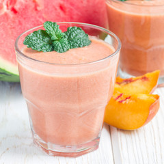 Watermelon, peach, mint and coconut milk smoothie in a glass on white wooden background, square