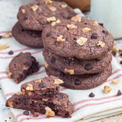Homemade chocolate cookies with walnuts and chocolate chips on the table, served with milk, square
