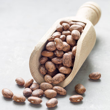 Uncooked dry pinto beans in a wooden scoop, square