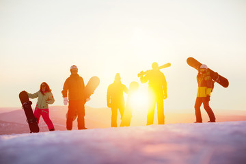 Group of serious friends with ski and snowboards against sunset
