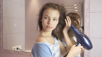 Beautiful teen girl dries hair a hairdryer in bathroom