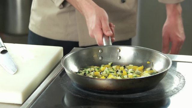 Hand of chef frying vegetables. Chopped eggplant, zucchini and pepper.