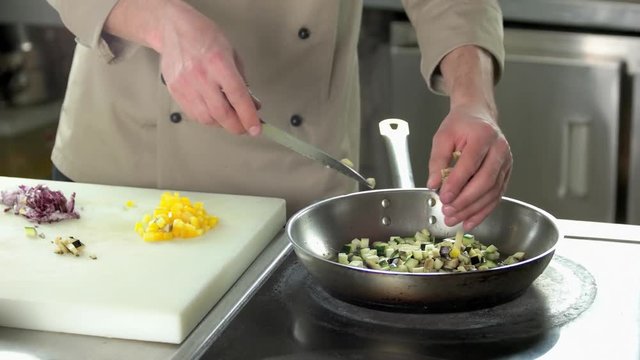 Hands of chef preparing food. Chopped vegetables in frying pan.