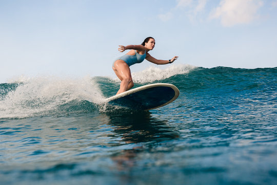 Young woman in bright bikini surfing on a board in ocean