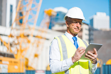 Construction manager controlling building site and tablet device in his hands