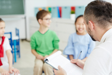 Fototapeta premium Side view of contemporary teacher listening to answers of his learners during examination