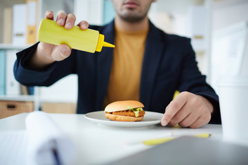 Office manager adding mustard from plastic bottle to his hamburger before eating it
