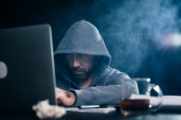 A male hacker is sitting behind a laptop and that he is typing
