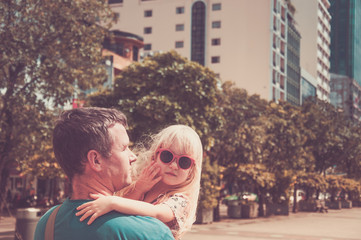 Photo toned in retro style. Little cute blond girl in sunglasses with dad in hands, looking into...