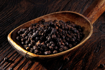  Black pepper in wooden spoon on wooden table