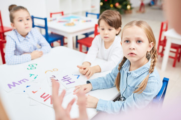 Fototapeta premium Attentive girl looking at teacher while listening to her explanation with groupmates on background