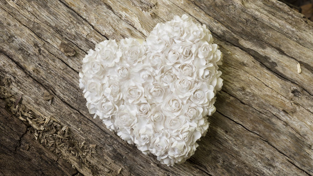 White heart made of little paper flowers on wooden table