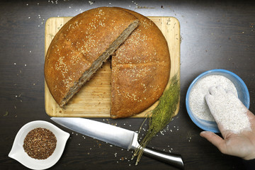 Home made integral bread with flax seeds, integral flour, dill and knife on wooden table. Woman holding the integral flour in her hand.