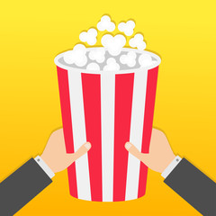 Two human businessman hands holding big popcorn box. Movie Cinema icon in flat design style. Pop corn. Fast food. Yellow gradient background.