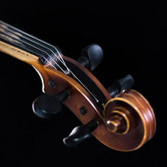 The extreme part of the violin fretboard is on a black background. A close-up of a tin box and a classic curl. For music news. A square picture.