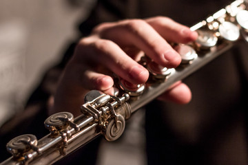 Part of a flute with the right hand of a man on a flute close-up. Shallow depth of field. Musical theme. Wind instrument. Modeling light. © romsvetnik