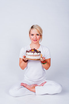 Yogi girl in a white suit holding a cake and wants to bite him. The concept of a healthy lifestyle, healthy sweets