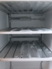 freezer compartment with an open door. The freezer covered with snow and ice is open for defrosting. In the refrigerator, snow and ice are melting, frozen on the walls and shelves.