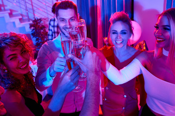 Group of happy young people raising glasses and toasting while celebrating holiday during house...