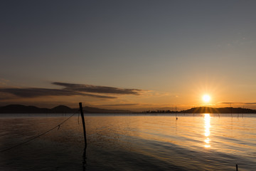 Fototapeta na wymiar Beautiful sunset over Trasimeno lake (Umbria), with sun coming down behind an island and some fishing nets in the foreground
