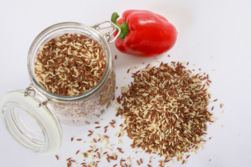 red (brown) rice in a transparent jar with lid yoke, Bulgarian pepper, white background