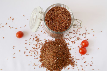 red (brown) rice in a transparent jar with lid yoke, cherry tomatoes, white background