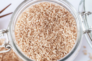 pink rice in a glass jar with a lid yoke, brown wooden sticks, white background