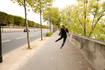 Autumn Parisian street, a girl in a black coat, blue jeans and sneakers in a jump