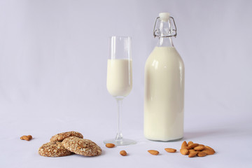 milk in a transparent glass bottle with a lid yoke, milk glass, homemade oatmeal cookies, almonds, white background