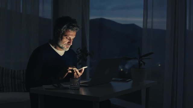 A mature man with smartphone working in home office.