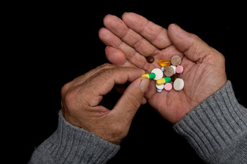 An elderly man holds a lot of colored pills in old hands. Painful old age. Health care of older people