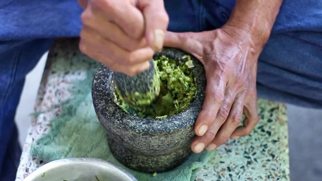 A male hand pounding many kinds of fresh herbs in a stone mortar. Male make curry paste in Thai cooking.