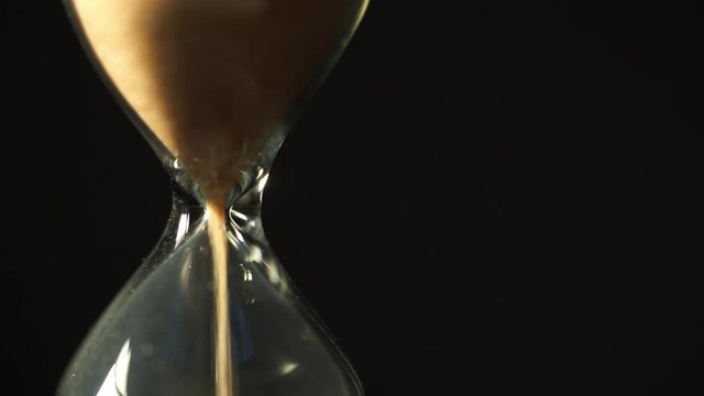 Sandglass, modern hourglass or egg timer showing the last second or last minute or time out. Isolated on black background with copy space.