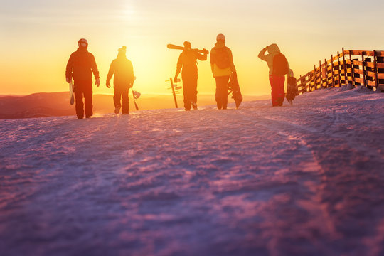 Friends with ski and snowboards walking to sunset