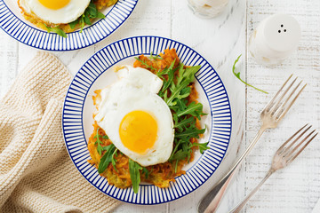 Fried egg with potato pancake, arugula and avocado on ceramic plate for breakfast on white wooden table background. Selective focus. Top view. Copy space.