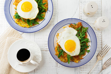 Fried egg with potato pancake, arugula and avocado on ceramic plate for breakfast on white wooden table background. Selective focus. Top view. Copy space.