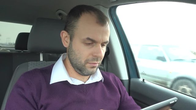 Businessman using a tablet while sitting inside car. Man with a tablet-pc in the  vehicle.