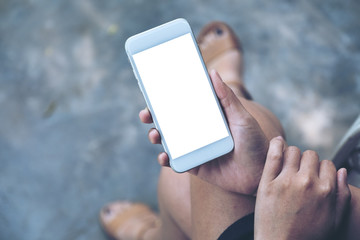 Mockup image of a woman sitting crossed leg and holding white mobile phone with blank desktop screen with concrete floor background