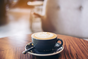 Closeup image of a blue cup of hot latte coffee with latte art on vintage wooden table in cafe