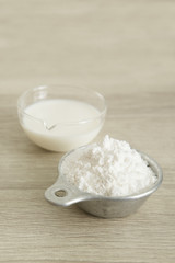 MILK AND FLOUR
White flour in a measuring cup and transparent jar with milk at the center on a wood table. 