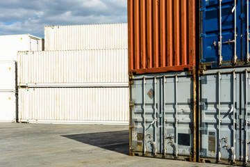 Worn intermodal containers stacked in a shipping yard with newer white pallet wide and refrigerated containers in the background.