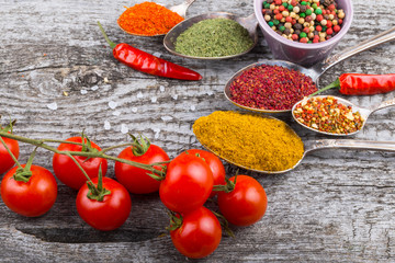 Bunch of cherry tomatoes, herbs, small bowl and antic metal spoons with different kinds of spices, sea salt and red hot chili peppers on old wooden board. Selective focus