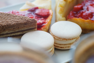 Bright sweet desserts are pastries and macaroons on a wooden table with hot chocolate and cocoa.