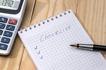 checklist on a notepad with pen and calculator on desk