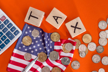 wooden cubes tax with flag, dollar, coin and calculator on orange background