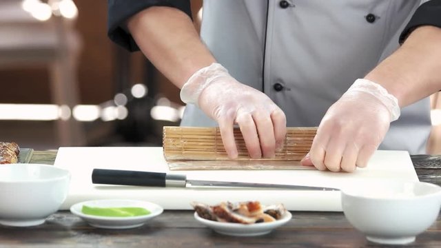 Sushi chef using bamboo mat. Japanese food preparation in restaurant.