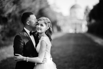 Lovely wedding couple walking along the green alley which leads to a church. Black and white photo.