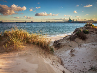 beach and sand dune with sea grass and clouds with the port of Algeciras in the background