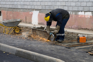 Close up of trained worker in protective workwear, gloves and glasses using angle grinder to smooth metal of profile pipe in workshop. Concentrated on metalwork skilled workman grinding steel parts