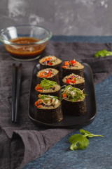 Vegan sushi rolls with quinoa, vegetables and soy-nut sauce on a black plate, black background. Vegan Healthy Food Concept.
